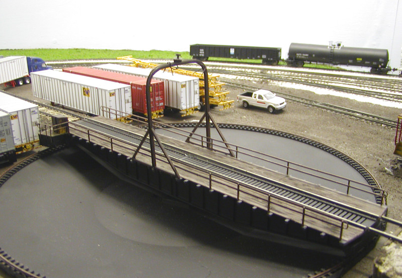 View of the new turntable looking southwest.  I made the following modifications to the Walthers kit:

- Removed the pit walls, since the prototype turntable is an above-ground type.
- Fabricated a rounded power arch and added conduit and a junction box beneath the power collector at the top.  Also added the V-shaped details seen in the photos.  Anyone know what those are?
- Scratchbuilt a new open-air operator's cabinet.
- Modified the handrails, removing one  railing and a number of stanchions from each side and adding rounded ends and a new section around the operator's cabinet.
- Weathered the deck using Bragdon powders, and then roughed it up and blended the powders using a wire brush attachment in my Dremel tool.