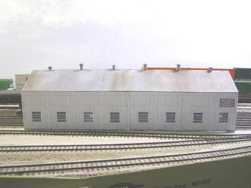 Looking west.  To better fit the scene, the overall structure was shortened by two sections, leaving only eight windows instead of the prototype's ten.  The roof vents were based on the prototype, with the #1 vent leaning to the west and the #3 vent missing its cap.  They were built using the roof vents from Walthers grain bins, with added peaks, inserted into Grandt Line 55 gallon drums.

The roof is Evergreen corrugated siding on the east slope seen in this photo, painted Rustoleum High Heat Flat Aluminum and weathered with oils, while the west slope is just sheet styrene painted Floquil Grimy Black and weathered, representing the prototype's tarred surface there.