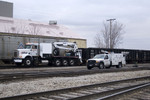 A rail mounted BNSF M-of-W Semi-truck shoves 3 gons east while a BNSF Ford tie gang support truck heads into the yard at Rock Island, IL.  March 25, 2009.