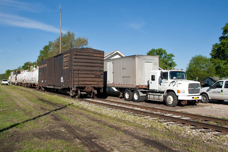 The Asplundh weed spray train on the left and Asplundh's supply truck on the right.  The trailer is one of the original roadrailer trailers, still tricked out with center railroad wheel between the 2 road axles!
