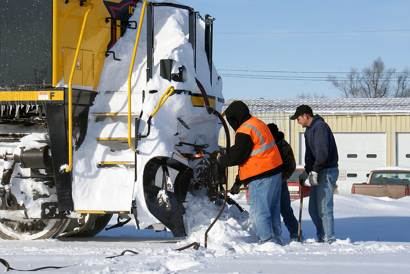 Workers use a torch, bar and maul to clean the packed snow from front coupler.
