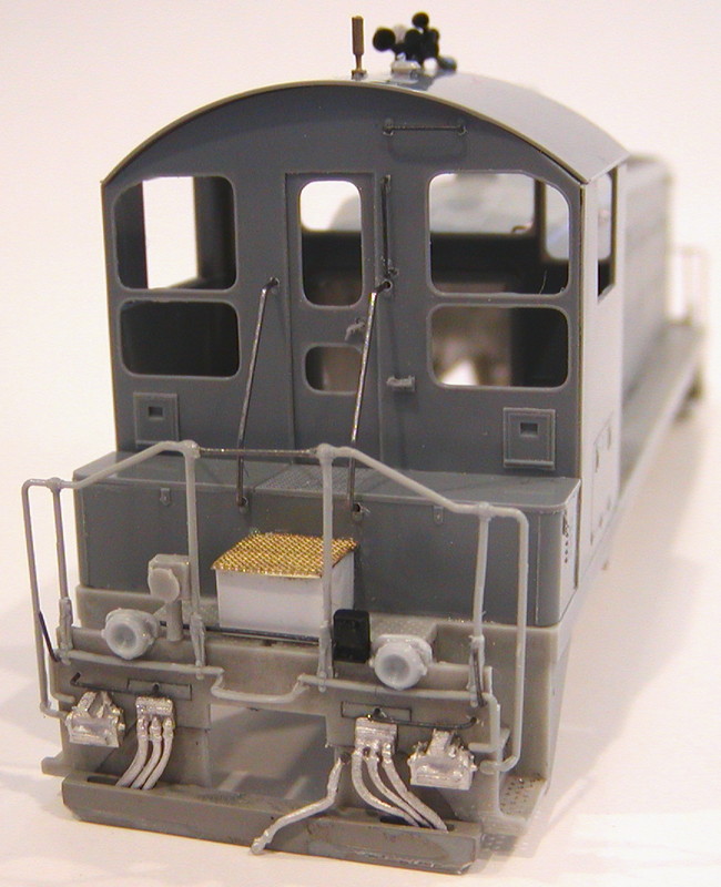 View of the rear cab face and pilot showing added ditch lights with conduit, styrene step box with Cannon treadplate, MU receptacles, spare coupler knuckles, MU and air hoses, pilot grab irons, coupler cut bar extensions, and MU hose pockets.