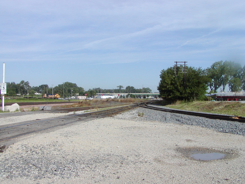 Prototype view looking west from CBGR crossing, with the Searle/Midwest Walnut spur on the right and BNSF and CBGR with the pink ballast toward the left.  In the distance, a BNSF Geep idles in KC yard.