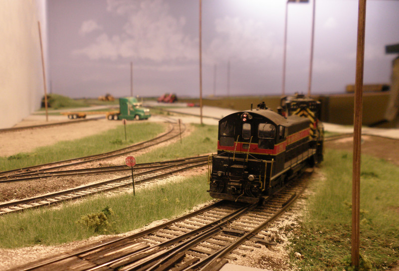 Looking west from the the CBGR grade crossing at the west end of Bluffs yard, with the BNSF main crossing from left to right, CBEC/CBGR to the left (pink ballast paralleling the IAIS), and BNSF KC yard west lead further in the distance, passing under the container chassis of the truck at the crossing.