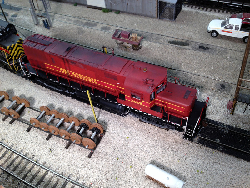 Top view of IAIS 850 at the Bluffs diesel pad.

This photo illustrates a number of the changes I made.  New radio and EOT antenna were added to the cab roof, and the beacon was moved forward, modified, and reprogrammed to better represent 850's strobe.  I also modified and relocated the horn, removed the sunshades and added a modified all-weather window to the engineer's side, added a plow, ditch lights, and coupler cut bar extensions to the pilots, and a small platform on the nose behind the sand fill cap.  On the cab face, I scraped off and patched over the class lights.

Paint and decal changes included the addition of "Work Safely" sticker decals to both ends of the frame on both sides.  The equipment trust information was painted over on the engineer's side frame, and all the handrails and stanchions were painted using a mix of decanted Rustoleum red and a few drops of Floquil light blue.  I painted over the yellow vertical stepwell edges with Floquil Engine Black.  

The 850 is former Green Bay & Western #323, so to model the prototype's worn patches over its former number, I decaled the long and short hood ends and cab sides with "323", then sponge-painted over them with a lightened version of the red paint mix mentioned above.  I also painted the patch over the 850's former "GBW" lettering on the long hood with that same color.

The fuel tank stains were done with Future floor wax.  Weathering was done with Pan Pastels and was applied pretty liberally.  After all, it's an Alco, so it had it coming. ;-)