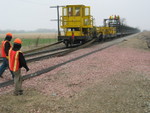 The new rail is anchored to a tie while the train pulls forward.